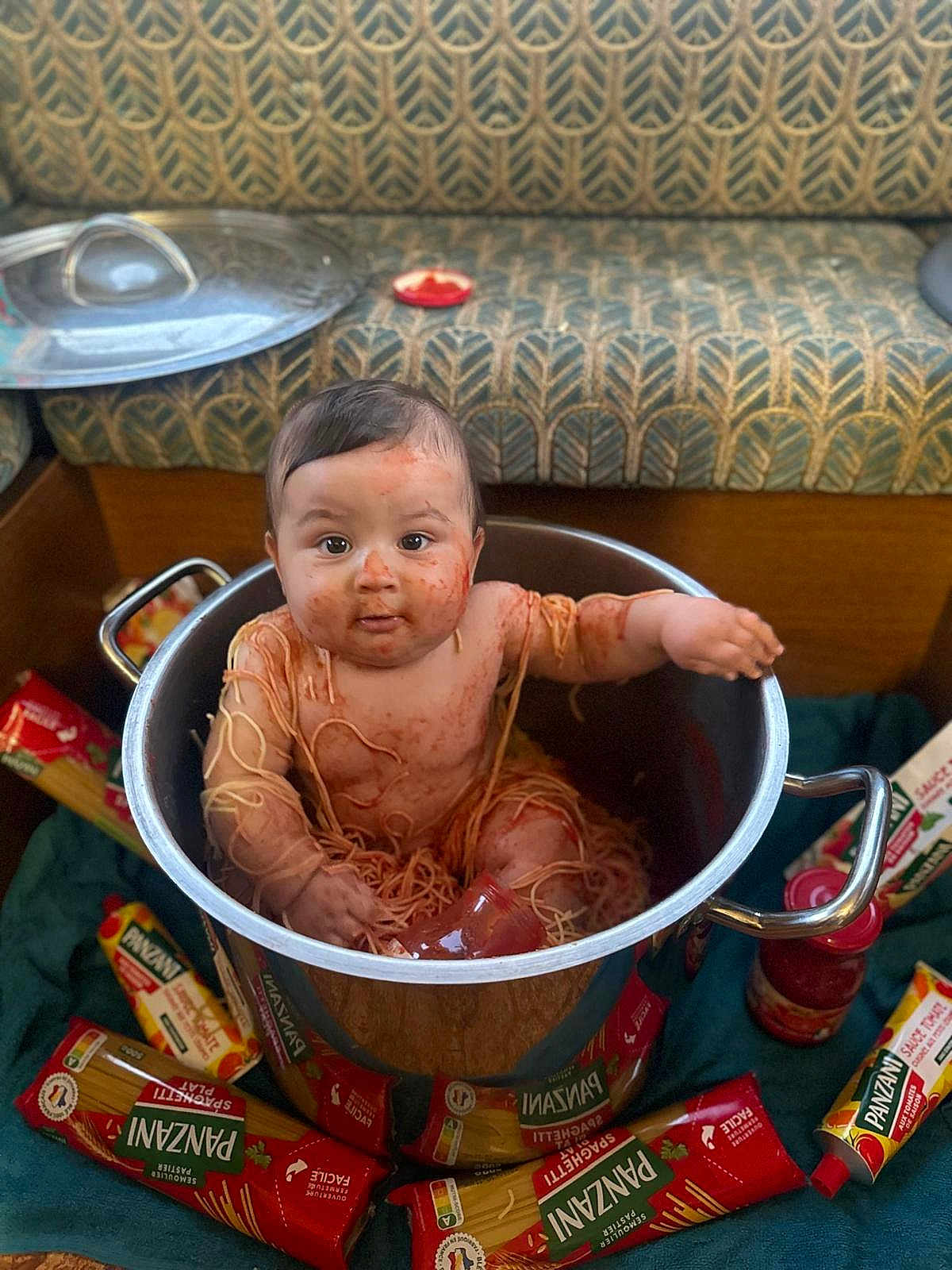 Keyvan a rejoint le concours — aidez-le/la à gagner de superbes lots ! baby, child, spaghetti, tomato_sauce, pot, pasta, kitchen, food, messy, cooking_pot, sitting, curious, indoors, couch, patterned_fabric, jar, packaging, cute, mess, funny