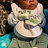 Jairus Wright is registered to the contest to win money with this photo: baby, bib, blanket, cartoon, child, clothing, cozy, cute, expression, face, green_pants, indoor, infant, leopard_print, mickey_mouse, mittens, person, portrait, sitting, white_socks