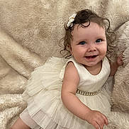 Adelina is registered to the contest to win money with this photo: baby, child, nine_months, dress, white_dress, smiling, hair_clip, curly_hair, fluffy_blanket, soft_texture, milestone, cute, infant, sitting, portrait, happy, indoor, toddler, young_child, celebration