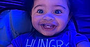 Zamir is registered to the contest to win money with this photo: baby, infant, child, smiling, happy, portrait, close_up, face, eyes, teeth, dark_hair, blue_lighting, indoor, seated, baby_seat, clothing, t_shirt, hunger, adult, photography