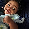 baby, child, infant, portrait, smiling, happy, face, curly_hair, wide_eyes, close_up, blanket, wrapped, lying_down, indoors, cozy, dark_background, hand, arm, bed, photography
