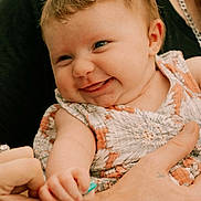 Ivory is registered to the contest to win money with this photo: baby, child, smiling, hand, holding, finger, curly_hair, dress, floral_pattern, portrait, cute, happy, skin, adult_hand, closeup, person, infant, playful, expression, warm