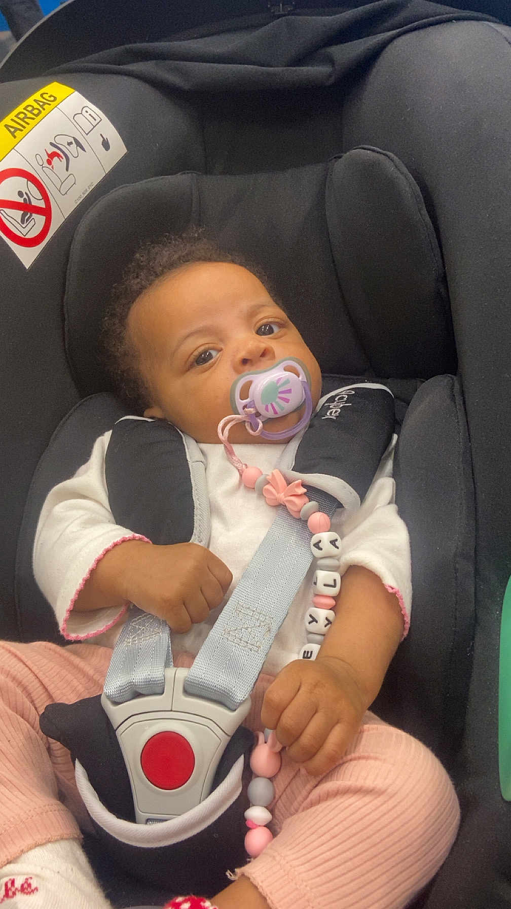 Neyla a rejoint le concours — aidez-le/la à gagner de superbes lots ! baby, car_seat, pacifier, beaded_toy, child, infant, seatbelt, pink_clothing, white_clothing, hands, face, eyes, curly_hair, safety, buckle, cute, indoor, closeup, portrait, child_safety