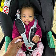 Neyla participe au concours pour gagner de l'argent avec cette photo : baby, child, car_seat, smiling, holding_hand, indoor, clothing, jacket, pants, socks, teddy_bear_patch, black_car_seat, safety_harness, adult_hand, wooden_floor, cute, portrait, infant, playful, seat_belt