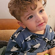 Nadim a rejoint le concours — aidez-le/la à gagner de superbes lots ! toddler, child, curly_hair, blue_shirt, orca_print, cucumber, hands, face, eyes, smile, indoor, cozy, soft_lighting, casual_clothing, seated, skin, young_child, cute, snack, portrait