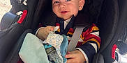 Lyham participe au concours pour gagner de l'argent avec cette photo : baby, child, car_seat, seatbelt, striped_sweater, red_pants, pacifier, soft_toy, blanket, smiling, blue_eyes, indoor, sunlight, comfort, infant, clothing, person, cute, happy, young