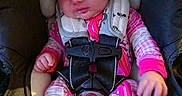 Nora is registered to the contest to win money with this photo: baby, newborn, child, infant, car_seat, safety_harness, bow, pink_clothing, sitting, portrait, face, hands, feet, indoor, vehicle, travel, buckle, colorful, baby_carrier, safe