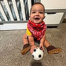 Maximilian is registered to the contest to win money with this photo: baby, child, infant, smiling, happy, sitting, soccer_ball, football, bandana, red_clothing, boots, carpet, nursery, crib, furniture, indoors, portrait, playtime, sports, cute