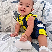 Maximilian is registered to the contest to win money with this photo: baby, child, infant, smiling, sitting, portrait, indoor, armchair, furniture, patterned_fabric, sportswear, yellow_clothing, navy_clothing, white_shoes, bracelet, short_hair, face, hands, legs, happy