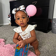 Amara joined the competition — help win amazing prizes! child, toddler, baby, portrait, sitting, indoors, carpet, pink_rug, balloon, piano, bow_headband, white_shirt, dress, book, colorful_book, numbers, curious, looking_at_camera, earrings, home
