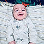 baby, smiling, onesie, infant, blanket, patterned_blanket, happy, cute, face, child, lying_down, hand, clothing, indoor, portrait, blue_eyes, young_child, baby_garment, infant_clothing, colorful_background