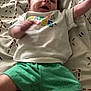 baby, child, infant, smiling, lying_down, clothing, shorts, shirt, blanket, pattern, happy, face, hair, arm, legs, indoors, floor, cute, person, toddler
