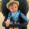 child, toddler, baby, smiling, portrait, stroller, hat, straw_hat, outdoor, sunlight, playful, happy, blue_eyes, colorful_clothing, tropical, travel, seated, harness, fashion, close_up