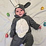 baby, costume, bunny, easter_eggs, blanket, cute, infant, lying_down, gray_clothing, white_background, holiday, festive, child, adorable, face, headwear, footed_pajamas, indoors, floor, playful