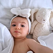 Aneli participe au concours pour gagner de l'argent avec cette photo : baby, child, headband, bow, stuffed_animal, bunny, toy, bed, blanket, white, soft, sleeping_area, face, portrait, cute, infant, toddler, closeup, indoors, resting