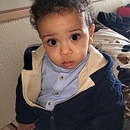 Sohan participe au concours pour gagner de l'argent avec cette photo : toddler, child, curly_hair, blue_shirt, navy_sweater, indoor, bed, striped_bedspread, window, curious_expression, person, young_child, sitting, hand, face, eyelashes, clothing, cozy, portrait, home
