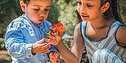 Sohan participe au concours pour gagner de l'argent avec cette photo : child, boy, girl, flower, outdoor, nature, sunlight, tree, curly_hair, braids, blue_shirt, striped_clothing, grass, playful, siblings, interaction, summer, park, daytime, happy