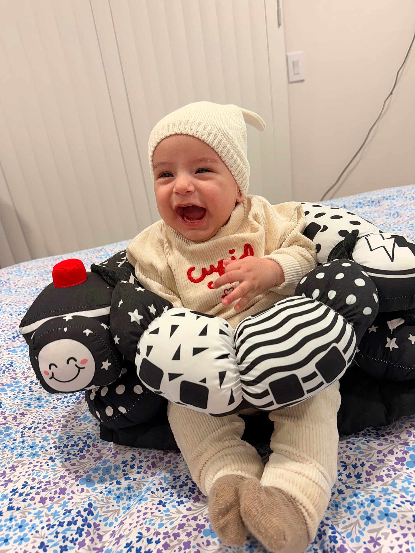 Raúl joined the competition — help win amazing prizes! baby, child, smiling, laughing, knitwear, hat, soft_toy, black_and_white, bedspread, floral_pattern, indoors, cute, happy, infant, person, sitting, cozy, plush, toy, clothing