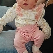 Lycia is registered to the contest to win money with this photo: baby, infant, child, headband, pink_clothing, white_clothing, mittens, sitting, person, indoor, couch, blanket, footwear, legs, cute, soft_fabric, portrait, baby_booties, holding, relaxed