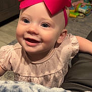 Ellie is registered to the contest to win money with this photo: baby, child, smiling, bow, pink, dress, face, indoor, blanket, toy, happy, headband, person, infant, cute, cheerful, portrait, furniture, floor, home
