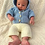 baby, infant, hoodie, knitted_clothing, blue_clothing, cream_pants, bare_feet, fist, curious_expression, soft_blanket, cozy, indoors, child, portrait, newborn, cute, warm, relaxed, lying_down, small_hands