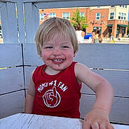 Xavier is registered to the contest to win money with this photo: child, toddler, smiling, messy_face, red_tank_top, outdoor, table, bench, wooden_furniture, daylight, blue_sky, building, people, blond_hair, happy, cute, face, person, casual_clothing, summer