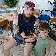 Dory joined the competition — help win amazing prizes! man, boy, dog, tattoos, cap, sunglasses, wooden_bench, indoor, plants, stroller, tile_floor, smiling, shorts, sleeveless_shirt, child, pet, casual, family, beard, home