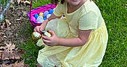 Rae Bates is registered to the contest to win money with this photo: child, girl, yellow_dress, grass, easter_eggs, basket, curly_hair, smiling, outdoor, spring, playful, greenery, leaves, fence, crouching, happy, holding, holiday, festive, daylight