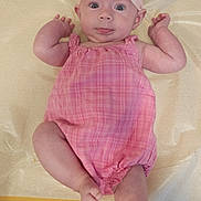 Olive is registered to the contest to win money with this photo: baby, child, infant, pink, romper, dress, headband, bow, plaid, lying_down, portrait, smiling, happy, indoors, changing_mat, baby_fashion, arms_raised, barefoot, face, photography