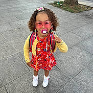 Jomana participe au concours pour gagner de l'argent avec cette photo : child, girl, fashion, pink_sunglasses, pacifier, braids, barbie_clip, yellow_cardigan, red_dress, white_sneakers, backpack, sidewalk, urban, street, trees, cars, concrete, outdoor, smiling, cute