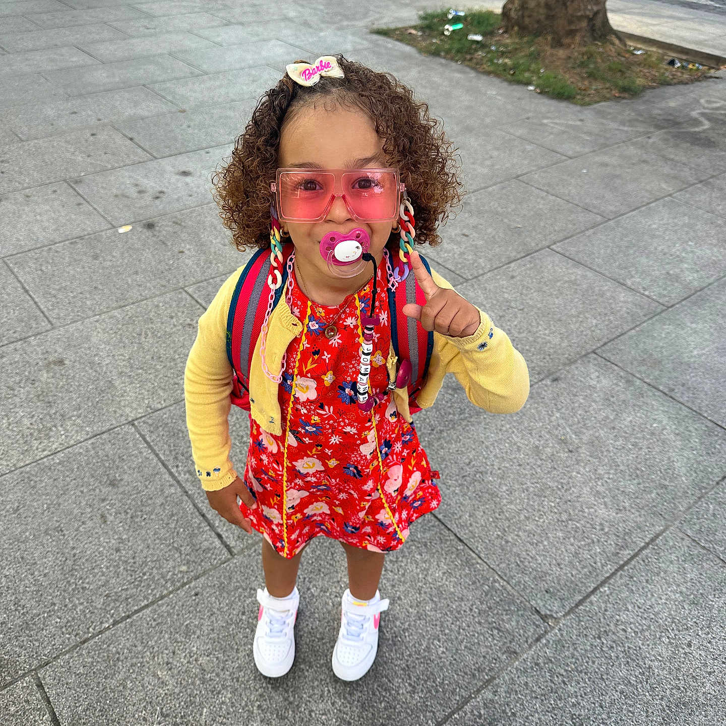 Jomana participe au concours pour gagner de l'argent avec cette photo : child, girl, fashion, pink_sunglasses, pacifier, braids, barbie_clip, yellow_cardigan, red_dress, white_sneakers, backpack, sidewalk, urban, street, trees, cars, concrete, outdoor, smiling, cute