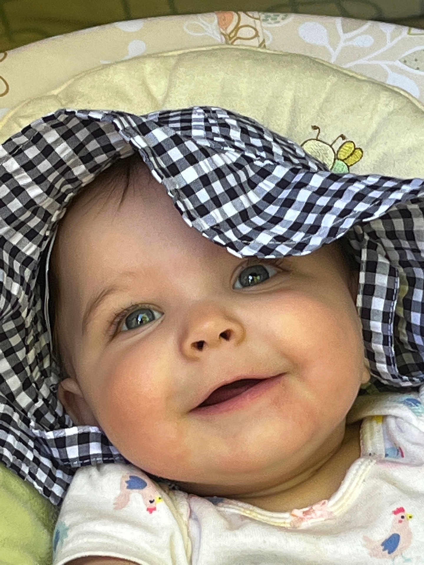 Zaiah is registered to the contest to win money with this photo: baby, smiling, face, hat, checkered_pattern, child, close_up, cushion, pattern, bee_design, clothing, cute, infant, cheeks, eyes, portrait, headwear, happy, baby_girl, lying_down
