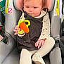 baby, car_seat, toy, child, infant, clothing, white_shoes, black_dress, tights, seat, child_safety, indoor, diapers, cute, holding, small_hand, face, car_interior, child_toy, infant_toy