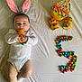 Akis participe au concours pour gagner de l'argent avec cette photo : baby, bunny_ears, carrot_toy, white_onesie, easter, chocolate_eggs, colorful, number_five, plush_toy, cute, lying_down, festive, celebration, infant, soft_toy, holiday, smiling, props, bed_sheet, sock