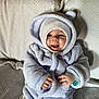 Akis participe au concours pour gagner de l'argent avec cette photo : baby, child, smiling, hood, coat, couch, indoor, cute, happy, warm_clothing, infant, face, hands, seated, plush, textured_fabric, portrait, cozy, home, apparel