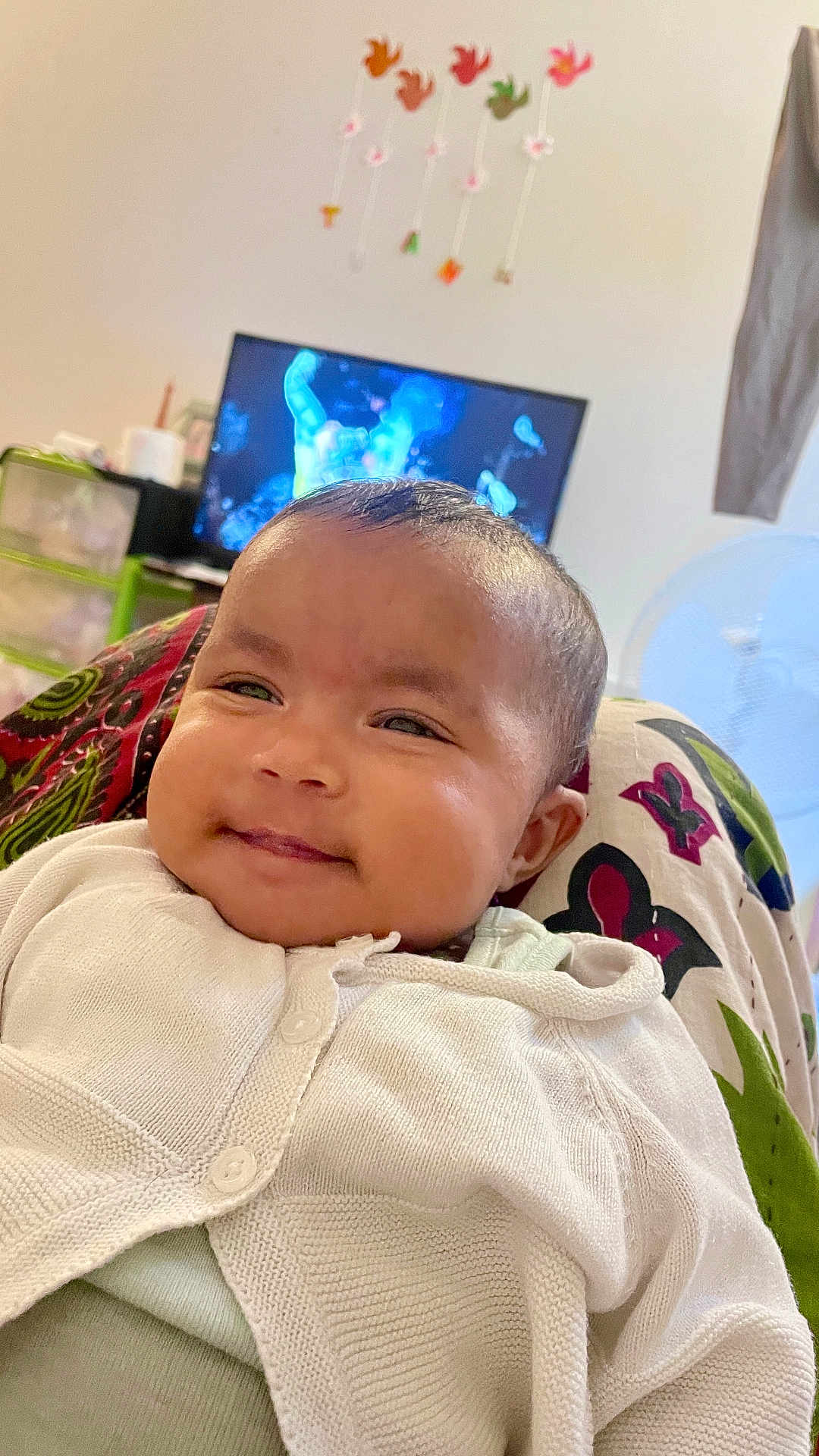 Tiana Talukder participe au concours pour gagner de l'argent avec cette photo : baby, smiling, white_cardigan, indoor, face, child, patterned_fabric, television, blurred_background, cozy, comfort, head, portrait, person, cute, infant, clothing, happy, closeup, relaxing