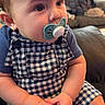 baby, pacifier, child, blue_clothing, checkered_pattern, sitting, indoor, couch, hands, face, curious, young_child, furniture, living_room, short_hair, cute, infant, portrait, looking_away, casual