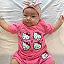 baby, infant, pink_clothing, headband, hello_kitty, cute, lying_down, white_sheet, child, toddler, smiling, shorts, tshirt, indoor, portrait, person, face, arms, legs, fashion