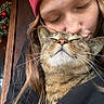 person, cat, tabby_cat, beanie, hat, kiss, hug, closed_eyes, content, indoor, wreath, holiday_decor, face, long_hair, warm_clothing, cozy, affection, pet, feline, love