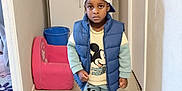 Ansry a rejoint le concours — aidez-le/la à gagner de superbes lots ! child, boy, indoor, hallway, clothing, cap, puffer_vest, mickey_mouse, sweatshirt, pants, sneakers, serious_expression, cabinet, chair, bucket, floor, wall, person, standing, portrait