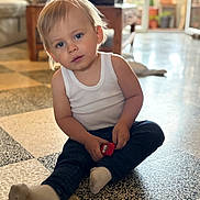 Henri participe au concours pour gagner de l'argent avec cette photo : child, toddler, toy_car, indoor, floor, sitting, white_tank_top, jeans, sock, curly_hair, blue_eyes, wooden_table, living_room, furniture, soft_light, patterned_floor, person, casual_clothing, cute, home