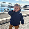 Henri a rejoint le concours — aidez-le/la à gagner de superbes lots ! toddler, child, outdoor, waterfront, blue_sky, jacket, timberland, brown_pants, white_shoes, sidewalk, railing, sunlight, person, face, curious, standing, casual_clothing, daylight, young_child, urban