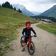 Elio a rejoint le concours — aidez-le/la à gagner de superbes lots ! child, mountain_bike, helmet, protective_gear, gloves, outdoor, mountain, path, gravel, nature, greenery, hill, trees, cloudy_sky, rural, adventure, sport, youth, cycling, landscape