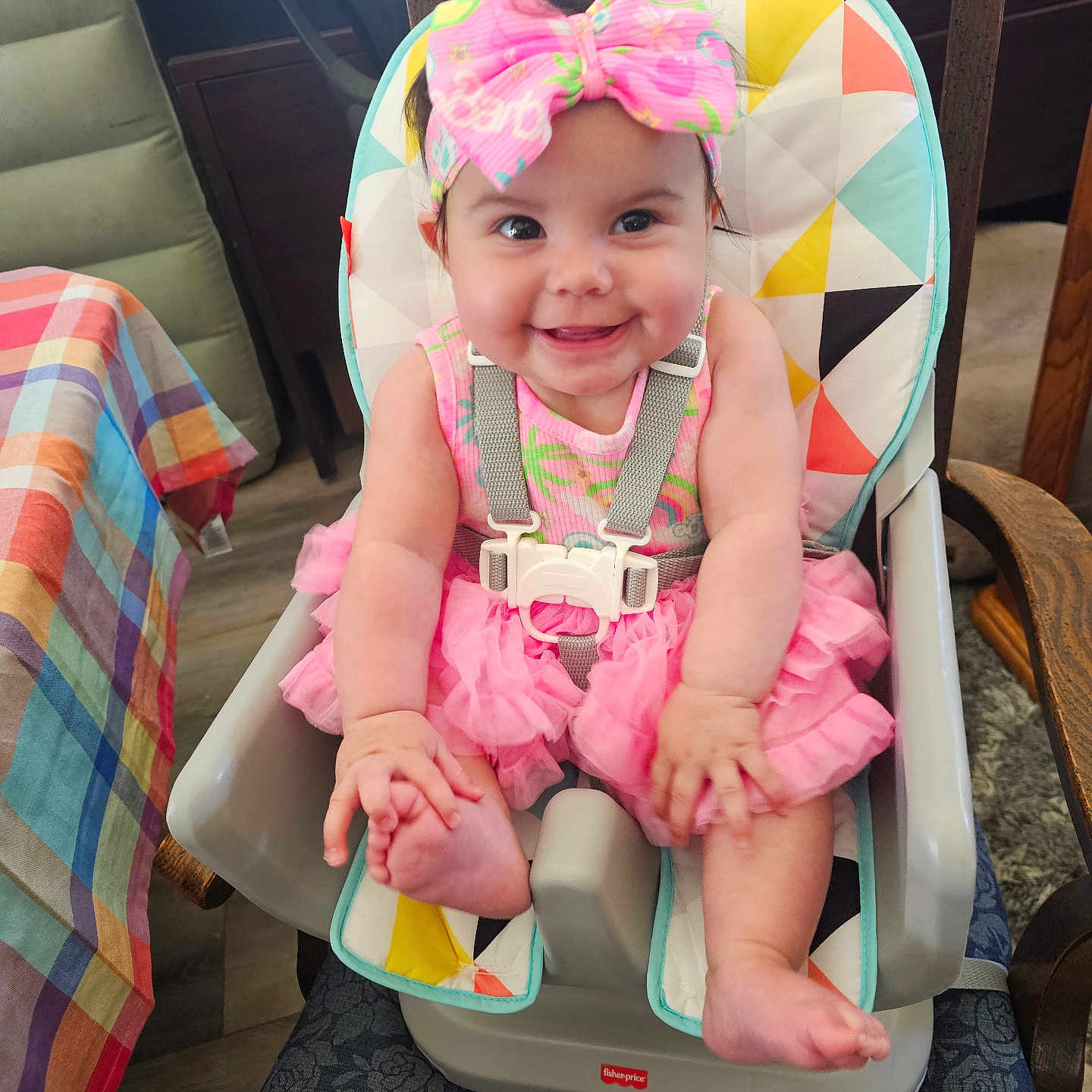 Lexilynn is registered to the contest to win money with this photo: baby, bow, child, colorful, cute, floor, furniture, happy, headband, high_chair, indoor, infant, person, pink_dress, playful, portrait, seatbelt, smiling, tablecloth, wooden_chair