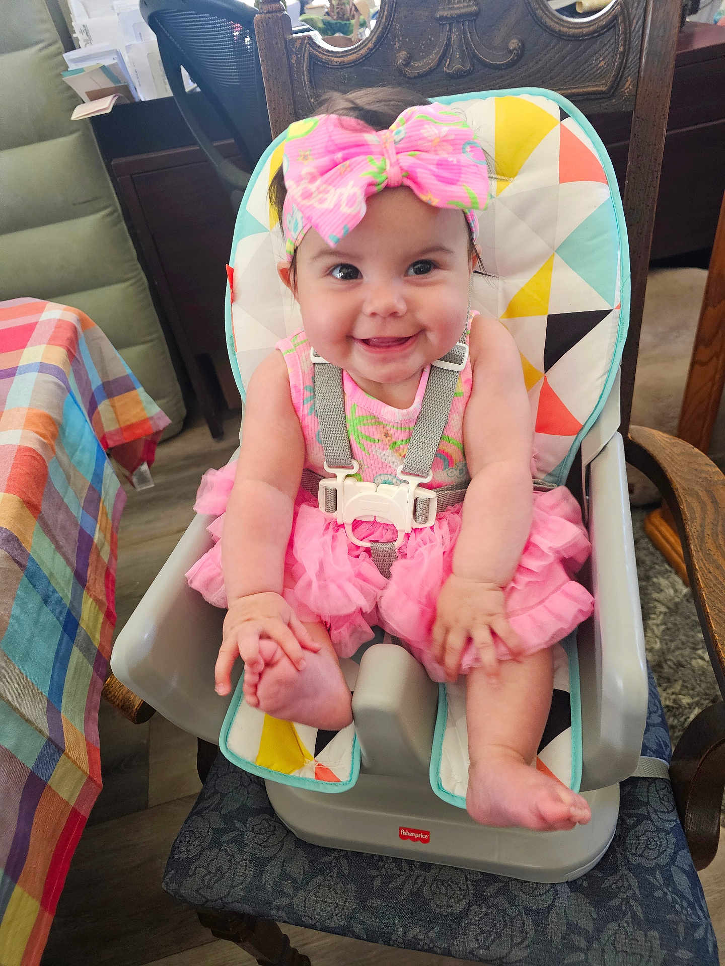 Lexilynn is registered to the contest to win money with this photo: baby, child, high_chair, smiling, pink_dress, headband, bow, indoor, furniture, tablecloth, wooden_chair, happy, infant, cute, seatbelt, floor, person, colorful, playful, portrait
