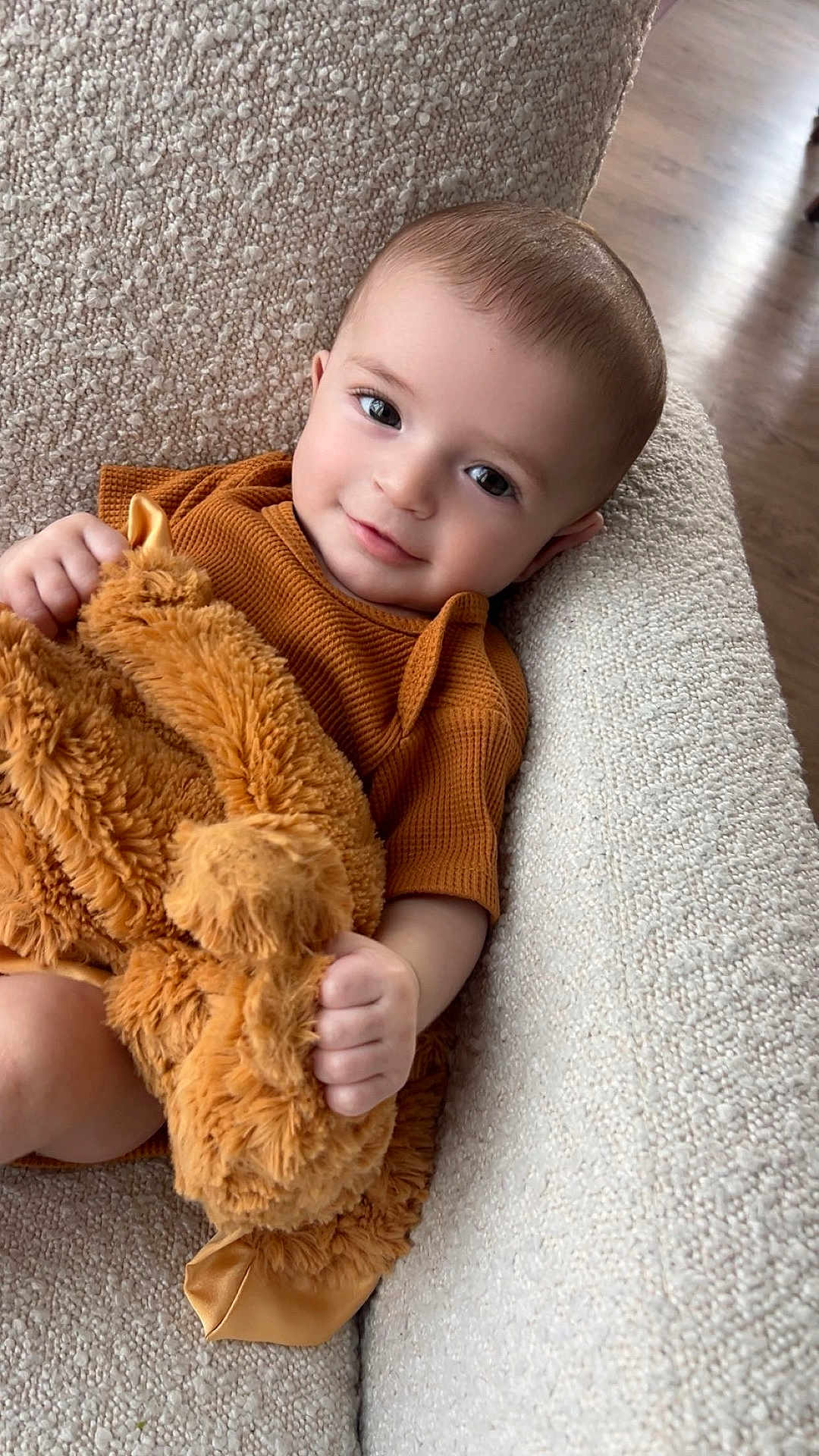 Cooper joined the competition — help win amazing prizes! baby, infant, child, smiling, plush_toy, stuffed_animal, couch, armchair, textured_fabric, brown_clothing, cozy, portrait, indoor, hand, eyes, hair, flooring, blanket, cute, relaxed
