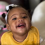 Aryel joined the competition — help win amazing prizes! toddler, child, baby, smiling, happy, face, headband, hair_puffs, yellow_bib, closeup, portrait, indoor, cute, person, skin, expression, young_child, joy, hand, cheerful