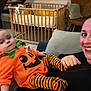 Louis participe au concours pour gagner de l'argent avec cette photo : baby, child, clothing, couch, crib, expression, face, furniture, happy, holding, home, indoor, living_room, person, pillow, portrait, pumpkin_costume, smile, striped_leggings, woman