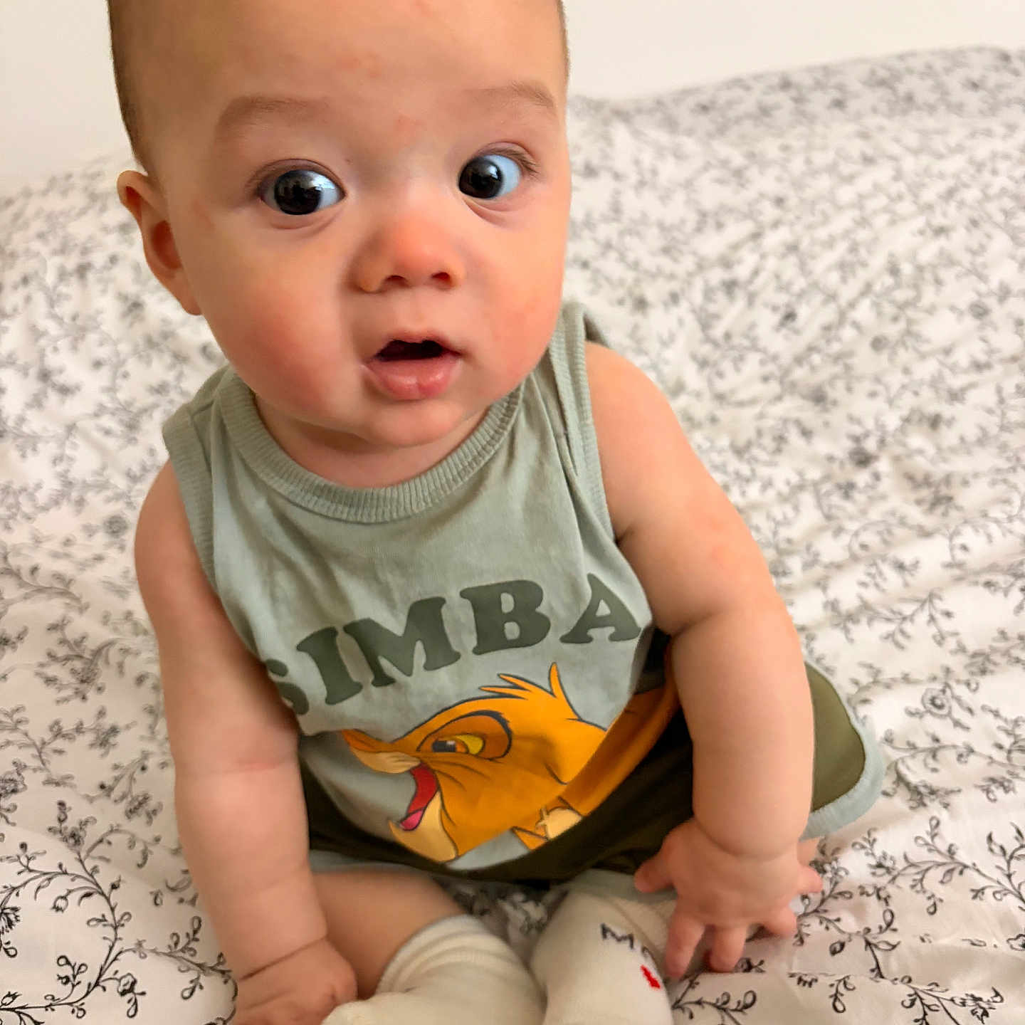 élian a rejoint le concours — aidez-le/la à gagner de superbes lots ! baby, bedspread, child, clothing, curious, cute, expression, eyes, face, foot, hand, indoor, infant, pattern, person, sitting, skin, socks, tank_top, young