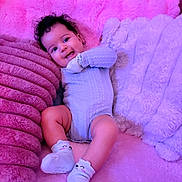 Serenity joined the competition — help win amazing prizes! baby, child, smiling, curly_hair, onesie, socks, pink, purple, plush, blanket, couch, happy, infant, person, cute, soft_texture, lying_down, cozy, indoors, portrait